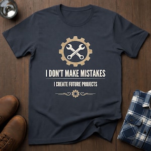 Könnte beinhalten: Marineblaues T-Shirt mit Zahnrad- und Schraubenschlüssel-Design. Der Text lautet "I DON'T MAKE MISTAKES I CREATE FUTURE PROJECTS". Das Shirt besteht aus weichem Material und ist für den Freizeitgebrauch geeignet.