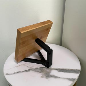 May include: A wooden phone stand with a black adjustable stand. The stand is made of bamboo and has a natural wood finish. The stand is designed to hold a phone in a vertical position.