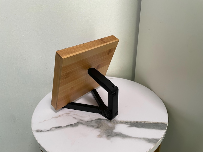May include: A wooden phone stand with a black adjustable stand. The stand is made of bamboo and has a natural wood finish. The stand is designed to hold a phone in a vertical position.