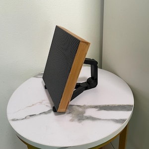 May include: A black speaker with a wooden frame and a black adjustable stand. The speaker is sitting on a white marble table.