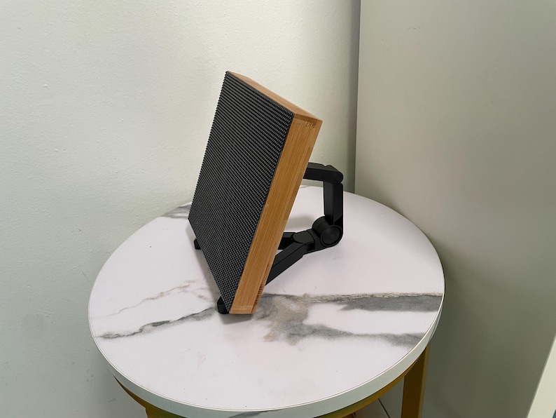 May include: A black speaker with a wooden frame and a black adjustable stand. The speaker is sitting on a white marble table.