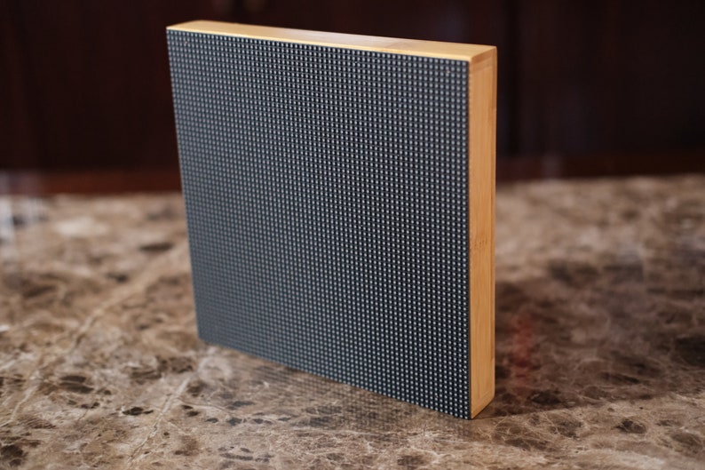 May include: A close-up of a black LED display panel with a wooden frame. The panel is made up of small, square LEDs that are arranged in a grid pattern.