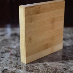 May include: A rectangular cutting board made of light brown bamboo. The board has a smooth surface and is made of multiple pieces of bamboo that are joined together.
