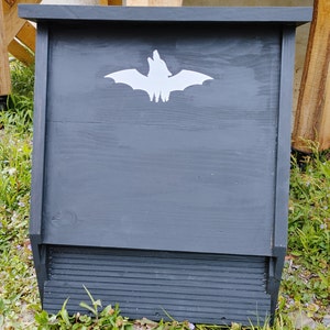 May include: A dark gray wooden bat house with a white bat silhouette on the front. The house has a hinged opening on the bottom.