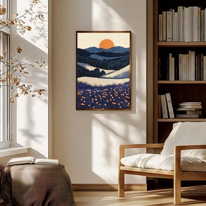 May include: A framed landscape art print depicting a sunset over rolling hills and a field of flowers. The artwork features a warm color palette with shades of orange, blue, and white. The print is displayed in a room with natural light.