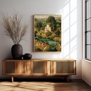May include: A framed vintage print depicts a serene landscape with a white domed building, a river, and lush greenery. The artwork is displayed above a wooden cabinet with a dark vase and decorative branches.