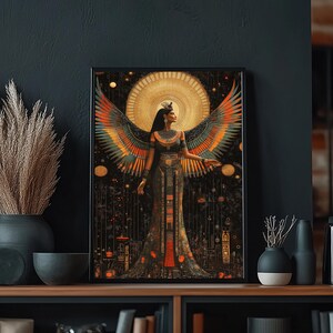 May include: Framed art print depicting a woman with large, colourful wings, set against a golden sunburst. The artwork has an Egyptian theme with intricate details and a dark, celestial backdrop. The print is displayed on a wooden shelf, with other decorative items.