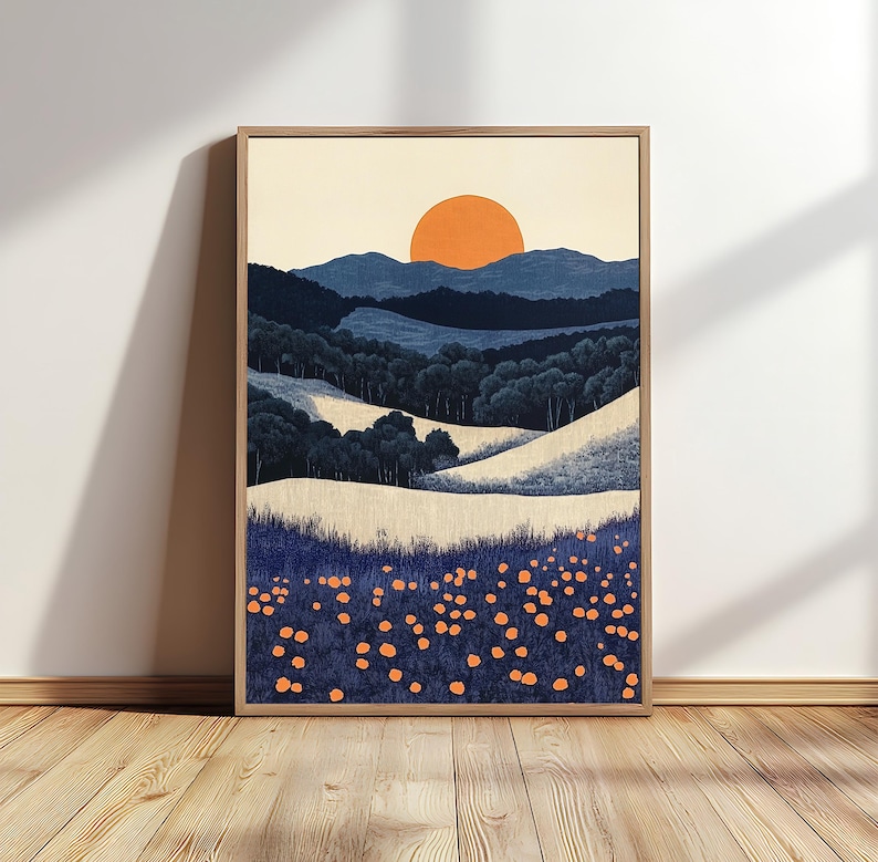 May include: Framed landscape art print featuring a stylized sunset over rolling hills and a field of orange flowers. The artwork uses a palette of blues, beige, and orange, creating a serene and natural scene. The print is displayed in a wooden frame.