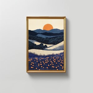 May include: Framed art print featuring a stylized landscape. The artwork depicts rolling hills, a forest, and a setting sun in shades of blue, white, and orange. The print is encased in a gold-colored frame.