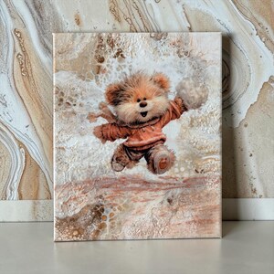 May include: A canvas print featuring a whimsical illustration of a teddy bear in a reddish-brown sweater and scarf, jumping with a fluffy ball. The background has a textured, abstract design in shades of brown and white.