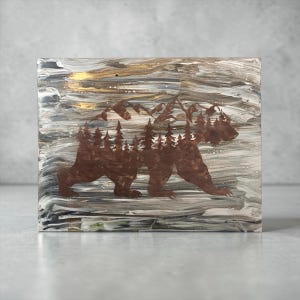 May include: A rectangular artwork featuring a brown bear silhouette filled with a forest and mountain scene. The background has a marbled effect with shades of gray, white, and gold. The artwork is a decorative piece.