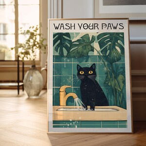 Puede incluir: Un gato negro con ojos amarillos se encuentra en un lavabo de ba&ntilde;o con un grifo dorado y agua corriendo. El texto "WASH YOUR PAWS" est&aacute; en la parte superior de la imagen. El fondo es una pared de azulejos verdes con plantas tropicales.