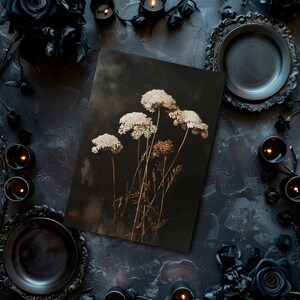 May include: A dark, moody still life featuring dried white flowers against a black background. The flowers are arranged in a vase and are surrounded by black candles and other decorative elements.