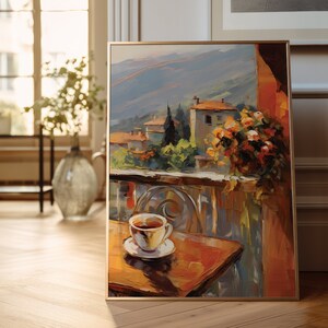 K&ouml;nnte beinhalten: Ein gerahmtes Gem&auml;lde einer farbenfrohen Landschaft mit einer Tasse Kaffee auf einem Tisch im Vordergrund. Die Landschaft zeigt ein kleines Dorf mit Geb&auml;uden und B&auml;umen und eine Bergkette im Hintergrund. Das Gem&auml;lde ist in einem goldenen Rahmen.