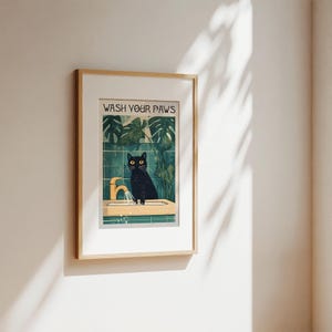 Puede incluir: Una impresi&oacute;n enmarcada con un gato negro lav&aacute;ndose las patas en un lavabo. La impresi&oacute;n tiene un fondo verde con plantas tropicales y el texto "WASH YOUR PAWS" en la parte superior.