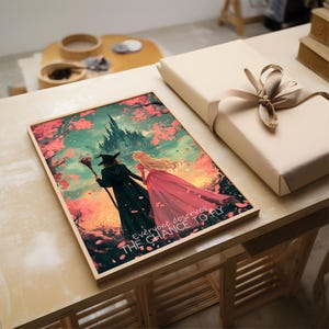 May include: A framed print with a fantasy illustration of two women walking away from a castle. The woman on the left is wearing a witch's hat and robe, and the woman on the right is wearing a pink dress. The background is a colorful sunset with pink cherry blossoms falling from the trees. The text "Everyone deserves the chance to fly" is printed at the bottom of the print.