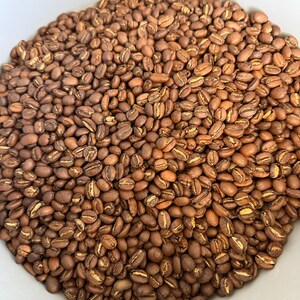 May include: A large collection of roasted coffee beans with a medium brown color. Each bean features a distinct central crease that is lighter in tone, showcasing the natural texture and oval shape of the roasted coffee product.