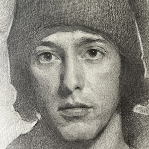 Op de afbeelding: Een gedetailleerde potloodtekening van een gezicht met een neutrale uitdrukking. De persoon draagt een donkere beanie en een donkere top. Het kunstwerk is in grijstinten, met zorgvuldige schaduw en textuur.