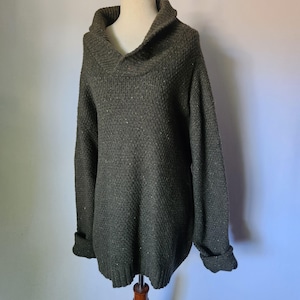 May include: A dark green sweater with a shawl collar and long sleeves. The sweater has a textured knit pattern and folded cuffs. The garment is displayed on a mannequin.
