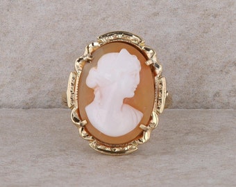 May include: A gold ring with a cameo featuring a woman's profile in white against a brown background.