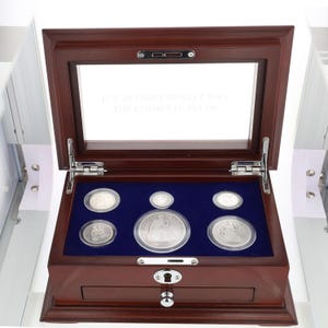 May include: A wooden box with a glass top containing a collection of silver coins. The box has a drawer and a lock. The coins are displayed in velvet-lined compartments. The text on the glass reads "The Seated Liberty Coin Collection".