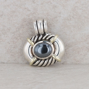 May include: A silver and gold pendant with a black gemstone in the center. The pendant has a rope-like design around the edge.
