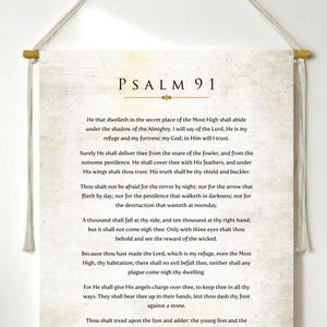 Puede incluir: Un colgante de pared crema con el texto del Salmo 91 impreso en negro. El texto se muestra en una fuente clásica. El colgante está suspendido de una varilla de madera con un cordón natural.