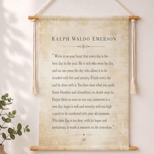 Könnte beinhalten: Ein beigefarbenes Wandbehang mit einem Zitat von Ralph Waldo Emerson. Der schwarze Text ist auf einer Rolle gedruckt, die von Holzdübeln gehalten und an einem Naturseil aufgehängt wird. Das Zitat beginnt: „Schreibe es dir ins Herz, dass jeder Tag der beste Tag im Jahr ist.“
