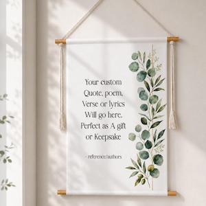 Peut inclure: Une tenture murale en tissu blanc suspendue par une tige en bois et une corde, ornée d'une illustration aquarelle de feuilles d'eucalyptus vertes sur la droite et du texte noir : Your custom Quote, poem, Verse or lyrics Will go here. Perfect as A gift or Keepsake - reference/authors.
