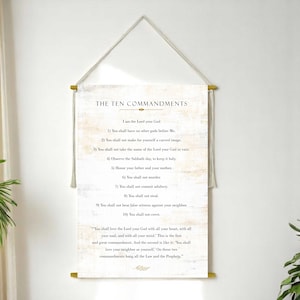 May include: A wall hanging featuring the Ten Commandments, printed on a cream-colored canvas. The text is in black, with a decorative gold-colored rod at the top and bottom. The canvas is suspended by a natural-colored rope.
