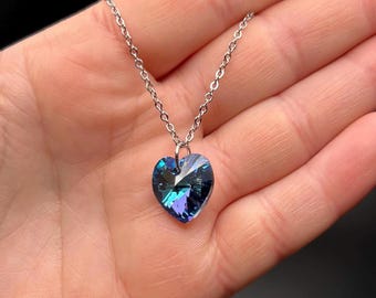 May include: A silver chain necklace with a blue heart-shaped pendant. The pendant has a faceted design and a dark blue color.