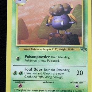 Peut inclure: Une carte de jeu de Pokemon représentant Gloom, un Pokemon de type Plante violet et vert avec 60 PV. La carte a un fond jaune et présente une illustration de Gloom dans un décor de forêt. Le texte de la carte décrit les attaques Poisonpowder et Foul Odor de Gloom.