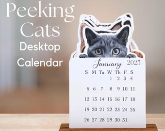 Könnte beinhalten: Ein Schreibtischkalender mit einem grauen Kätzchen, das über die Oberseite schaut. Der Kalender zeigt den Monat Januar 2025 mit den Wochentagen und Daten deutlich an. Der Kalender steht auf einem Holzsockel, mit den Worten "Peeking Cats Desktop Calendar".