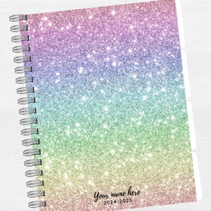 May include: A rainbow glitter planner with a silver coil binding. The cover has the text "Your name here 2024-2025".