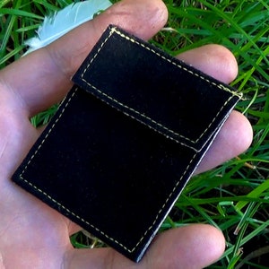 Può includere: Una pochette in velluto nero con cuciture gialle. La pochette è piegata a metà ed è tenuta in una mano.
