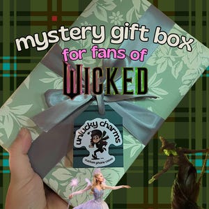 May include: A gift box wrapped in patterned paper and tied with a grey ribbon. Text on the box reads "mystery gift box for fans of WICKED". A tag says "unlucky charms custom phone cases". The tag features a cartoon character.