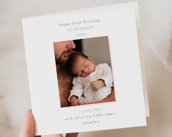May include: A white greeting card with a photograph of a baby held by an adult. The card reads "Happy first Birthday AS MY DADDY 2026" and "I LOVE YOU with all of my little heart, Amelia x."