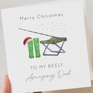 May include: A white card with a Christmas greeting that says "Merry Christmas to my Reely Amazing Dad". The card features a fishing rod, a folding chair, and a pair of green rain boots with Santa hats.