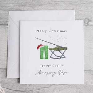 May include: A white Christmas card with a fishing rod, green boots, a folding chair, and the text "Merry Christmas To My Reely Amazing Papa".