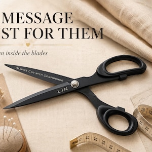 May include: Matte black metal scissors featuring the engraved text "ALWAYS CUT WITH CONFIDENCE" on one blade and "LIN" near the pivot. The scissors are positioned alongside a beige measuring tape, a pin cushion, and spools of thread.