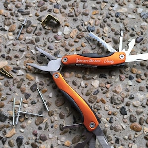 May include: Orange and silver multi-tool with a black handle. The tool has a variety of blades and tools, including pliers, a knife, a saw, and a screwdriver. The handle is engraved with the words "You are the best - Daddy".