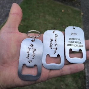 May include: Three silver bottle opener keychains with engraved messages. The first keychain says "Daddy's Keyring" with a heart and a key symbol. The second keychain says "Cheers To You, Daddy!" The third keychain says "James DRINK LESS. DRIVE SAFELY. COME BACK EARLY!"