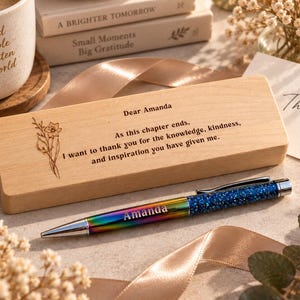 May include: A rectangular light wood box engraved with a floral design and the text Dear Amanda, As this chapter ends, I want to thank you for the knowledge, kindness, and inspiration you have given me, paired with a rainbow metallic pen labelled Amanda.