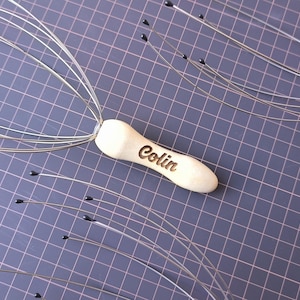 Op de afbeelding: Twee zilveren hoofdmassagers met houten handvatten. Het handvat van één massager is gegraveerd met de naam "Colin".