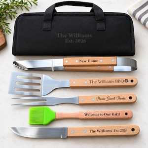 May include: A set of five stainless steel grilling tools with light wood handles, each engraved with text including New Home, The Williams BBQ, Home Sweet Home, Welcome to Our Grill, and The Williams Est. 2026, stored in a black zippered carrying case.