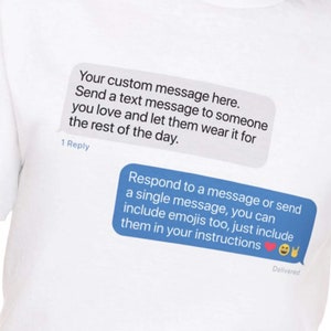 May include: White t-shirt with a blue text message bubble graphic that says "Your custom message here. Send a text message to someone you love and let them wear it for the rest of the day."  The text bubble graphic is a common design element used in mobile messaging apps.  The text bubble graphic also says "1 Reply".  Below the first text bubble graphic is a second blue text bubble graphic that says "Respond to a message or send a single message, you can include emojis too, just include them in your instructions."  The second text bubble graphic also includes a red heart emoji, a yellow smiley face emoji, and a rock on hand emoji.  The second text bubble graphic also says "Delivered".