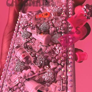 May include: Pink phone case with a glittery, resin-filled design. The case is decorated with miniature bottles of alcohol, money, and hearts. The case is covered in rhinestones.
