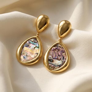 May include: A pair of gold-toned drop earrings featuring a smooth, polished teardrop-shaped top connected to a larger, rounded teardrop base. Each base is inlaid with iridescent, multi-colored abalone shell displaying shades of green, pink, and blue.