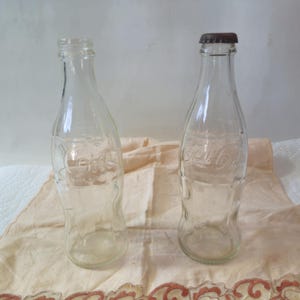 2 Vintage Coca Cola Bottles, one with original lid, rusted