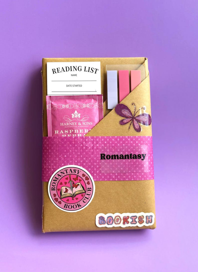 May include: A brown paper-wrapped gift box with a pink polka-dot band labeled "Romantasy." It contains a reading list, tea, and sticky notes. A butterfly sticker and a "Romantasy Book Club" sticker are also visible. The word "BOOKISH" is also visible.